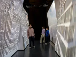 Three people standing in a museum exhibit showcasing architectural views of buildings in 3D.