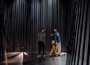 Three people standing in front of a modern art installation featuring a curtain of metal rods