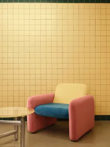 A modern living room with a pink and blue armchair against a yellow tiled wall.