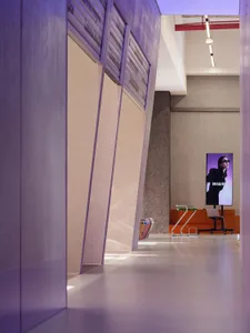A modern lobby with concrete walls, floors, and ceiling, featuring a digital screen displaying a woman in sunglasses.