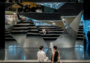 Two people sitting in a modern performance space with reflective mirrors.