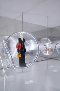 A modern retail display featuring a mannequin dressed in black and yellow clothing, holding a red bag, suspended inside a tra