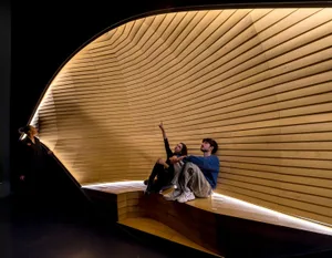Three people exploring a modern, industrial-style interior with curved wooden walls and bench seating.