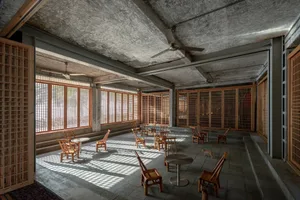 A minimalist coffee shop interior made of concrete material, with wooden furniture and large windows allowing natural light.