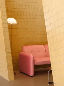 A minimalist restaurant interior with yellow-tiled walls, a pink armchair, and a floor lamp.