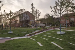 A modern park featuring a green grassy area with a brick pathway and a render of a building in the background.
