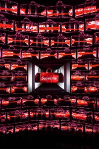 從側面觀看一面由透明 plexiglass 製成的零售袋牆，袋身帶有紅色點綴並印有「Supreme」字樣。