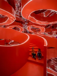 Children sitting on stairs surrounded by red metallic walls with neon lighting and reflective surfaces.