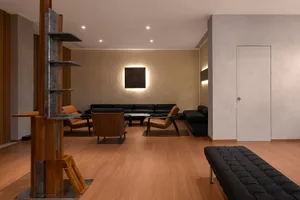 Modern minimalist living room featuring black leather furniture and wooden accents on a brown wooden floor.