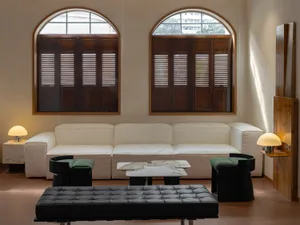 A modern living room with a white modular sofa, black tables, and green cushions next to large arched windows with wooden shu