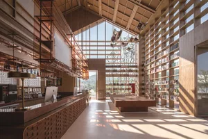 A modern interior featuring a restaurant, bar, and library with walls of wood and concrete, full-height glass windows, and pe