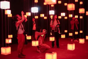People exploring an immersive lighting installation with paper lanterns hanging in a dark room.