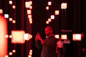 A minimalist art installation featuring suspended cubes of light against a dark background.