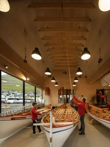 People working inside a boat shop with wooden boats and shelves