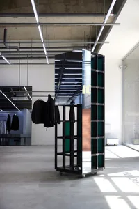 A modern metal clothing display system with wheels, placed in an empty interior space with a concrete floor and visible pipes