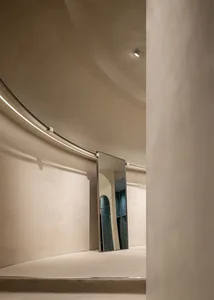 A modern interior space with curved walls and neutral materials, including a reflective mirror.