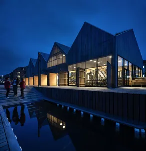 Modern indoor architecture with wooden exterior, illuminated by lights at dusk.
