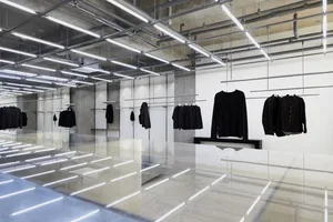 Modern, minimalist retail interior featuring industrial design elements and black clothing on display.