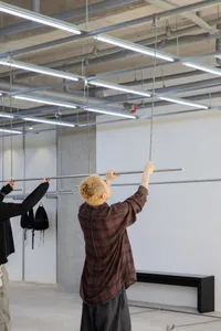 A person adjusting a metal rod in a modern interior space with cables hanging from the ceiling.