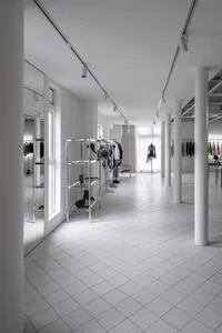 簡約風格的服飾店，鋪設白瓷地板並搭配白牆，展示架與人體模特兒陳列服裝。