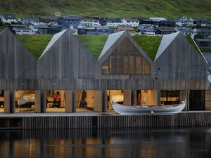 Modern wooden architectural structure with green roofs and boats docked in the water.