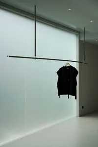 A minimalist clothing display featuring a single black garment hanging from a suspended rod.