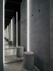A minimalist interior design space featuring a concrete bar counter, with sleek, linear lighting fixtures and cushioned stool