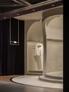 A minimalist retail display featuring a white garment on a concrete platform with a purple curtain backdrop.