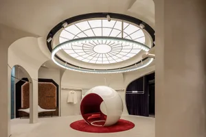Modern retail shop interior featuring a circular glass space with a white and red circular pod on a red carpet.