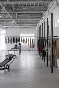 Modern retail clothing shop showcasing minimalist design with metal racks, glass walls, and concrete floors.