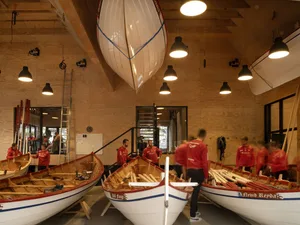 People working in a modern boating center with boats, oars, and wooden structures.