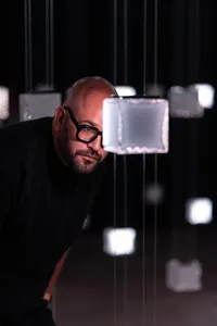 Person leaning on a modern glass box installation in a dark space.