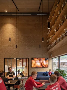 Modern cafe with wooden interiors, featuring hanging lamps and a flat-screen TV.
