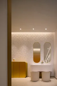 Modern bathroom design featuring a white concrete vanity with two curved mirrors above it, a gold cabinet, and a textured whi