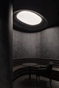A minimalist coffee shop with a concrete ceiling and circular window.