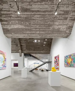現代藝術博物館內部，露出混凝土天花板，牆面懸掛大型藝術作品，並設有白色座位區。