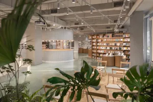 A modern cafe lounge with concrete flooring and wooden furniture, featuring green plants and a central circular bar.