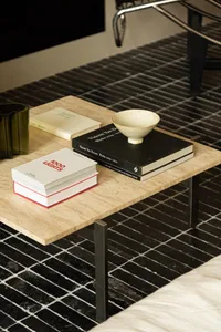 A modern coffee table featuring a marble top and steel legs, with a bowl and books on top, against a black and white tile flo