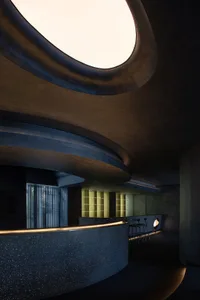 Modern hotel lobby interior featuring a sleek, curved concrete reception desk with a skylight overhead.