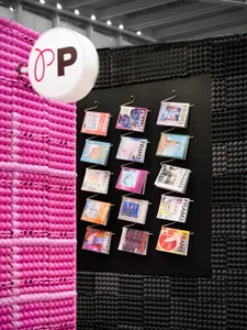A modern magazine display featuring various colorful publications with a pink and black textured backdrop.