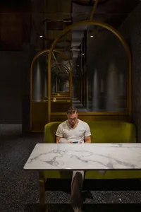 Man sitting at a modern cafe with black and golden metallic furniture, white marble table, and decorative lighting.