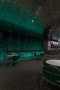 A modern restaurant bar with a textured concrete ceiling and green lighting.