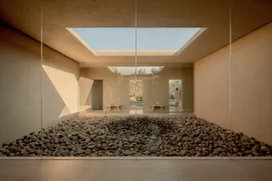 A minimalist room with concrete walls, glass walls, and a stone floor, featuring a skylight.