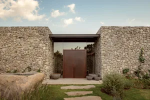A modern house exterior made of stone with a large glass door.