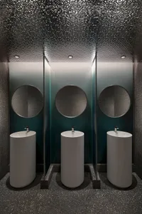 Modern bathroom interior with white circular sinks, terrazzo flooring, and round mirrors.