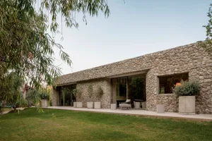 A modern residential building with a stone exterior, large windows, and a lush garden.