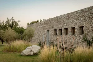A modern stone building exterior at dusk, surrounded by natural vegetation.