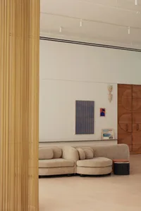 A modern living room with a beige sofa set against a white wall, featuring abstract art and a wooden cabinet. The floor is li
