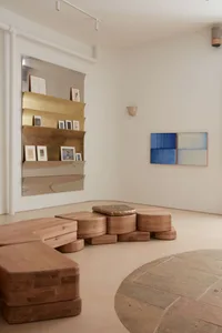 A minimalist art gallery featuring abstract wooden sculptures and colorful paintings displayed on a wall.