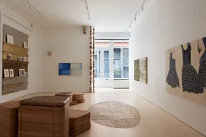 A modern art gallery interior with wooden furniture, sculptures, and art displayed on the walls.